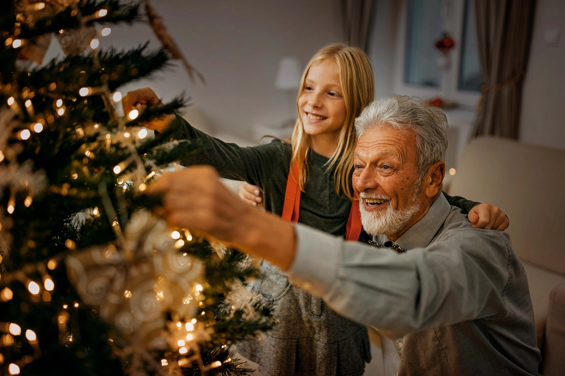 Ein älterer Mensch und ein Kind schmücken gemeinsam einen leuchtenden Weihnachtsbaum.